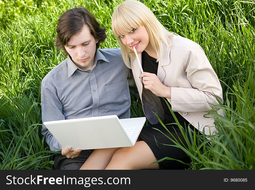 A young business man and business woman working on laptop in nature on the grass field. A young business man and business woman working on laptop in nature on the grass field