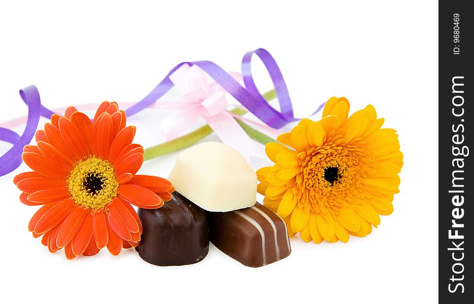 Luxury chocolates with Gerbera flowers and festive ribbons for the celebration of a special day. Isolated on white. Luxury chocolates with Gerbera flowers and festive ribbons for the celebration of a special day. Isolated on white.