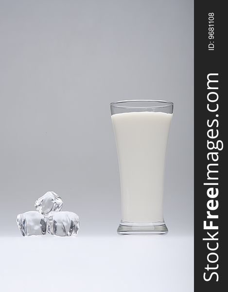 A glass of milk with ice on gray  background. A glass of milk with ice on gray  background