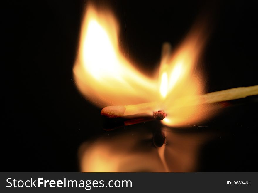 A match bursting into flames, isolated on a black reflective surface. A match bursting into flames, isolated on a black reflective surface