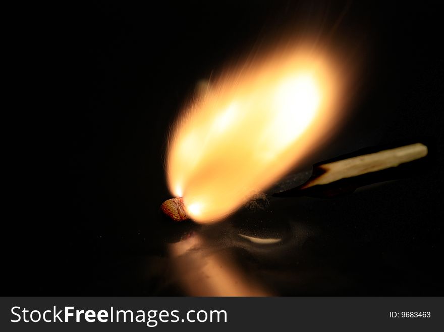 A match bursting into flames, isolated on a black reflective surface