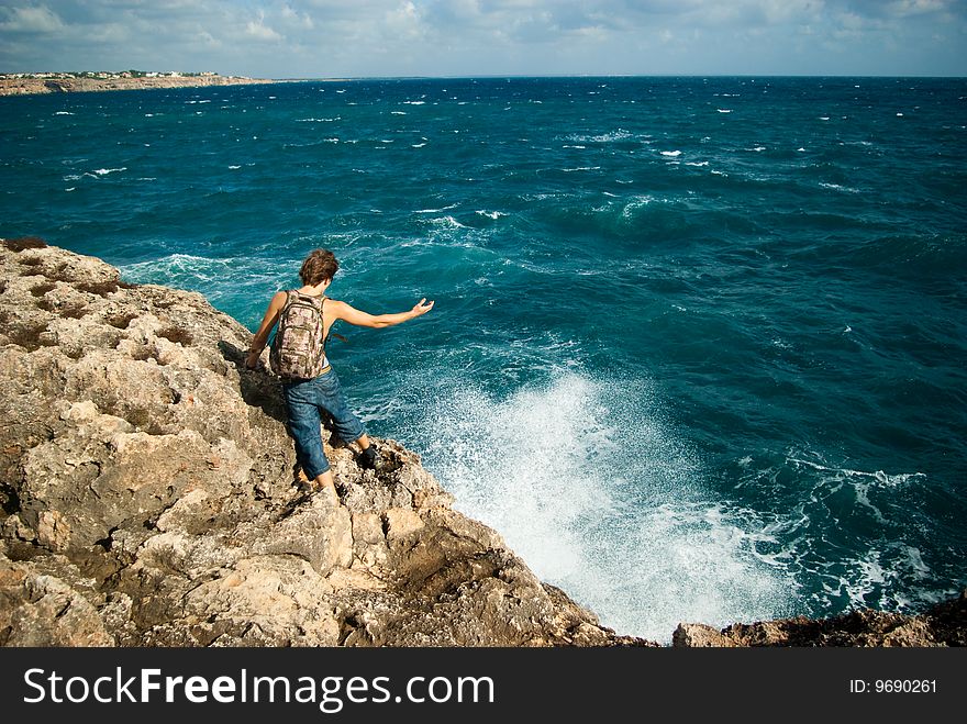 Young hiker with a backpack holds out a hand to the sea. Young hiker with a backpack holds out a hand to the sea