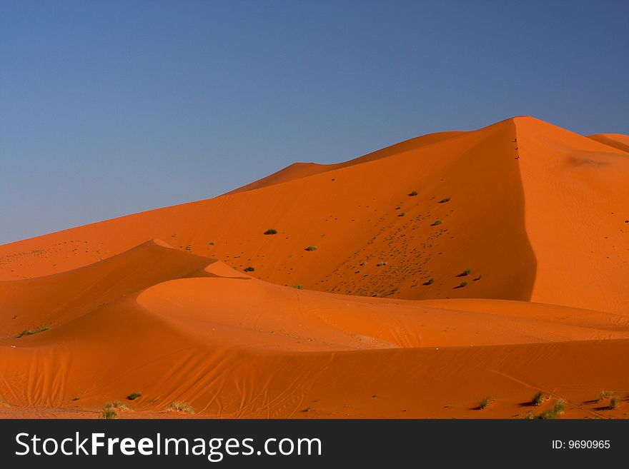 Three men are climbing at the top of the highest desert dune. Three men are climbing at the top of the highest desert dune