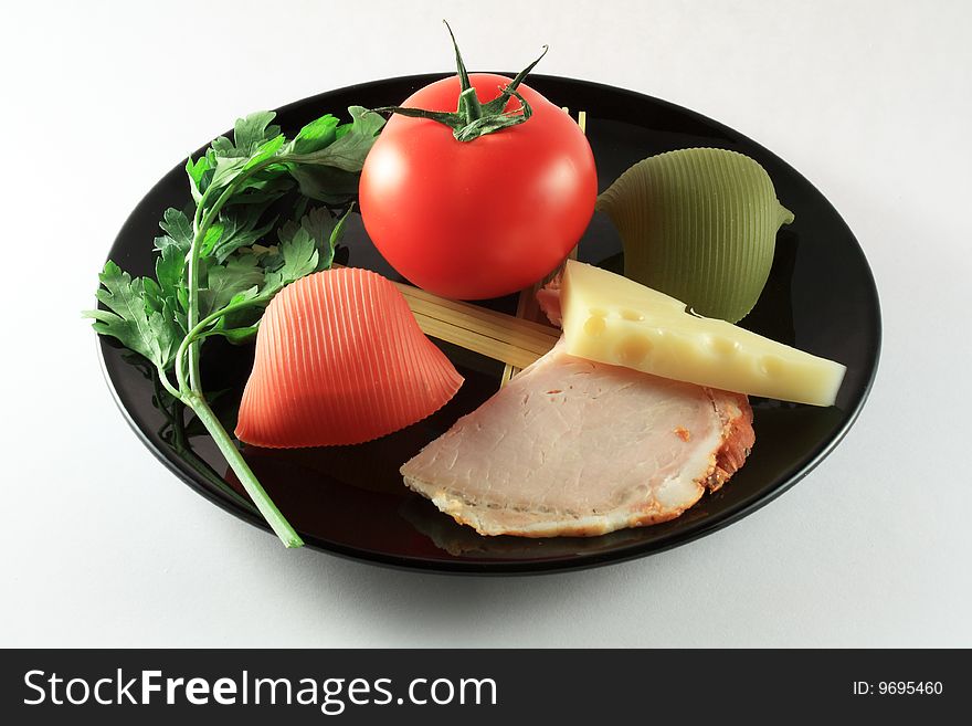 Ham, green parsley, cheese, pasta and tomato on a black plate. Ham, green parsley, cheese, pasta and tomato on a black plate