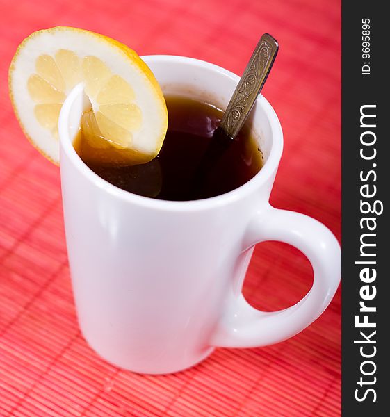 White cup with black tea and piece of lemon