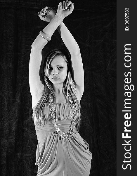 Young female fashion model holding her arms up crossed over her head looking at the camera against a charcoal back drop. Young female fashion model holding her arms up crossed over her head looking at the camera against a charcoal back drop.