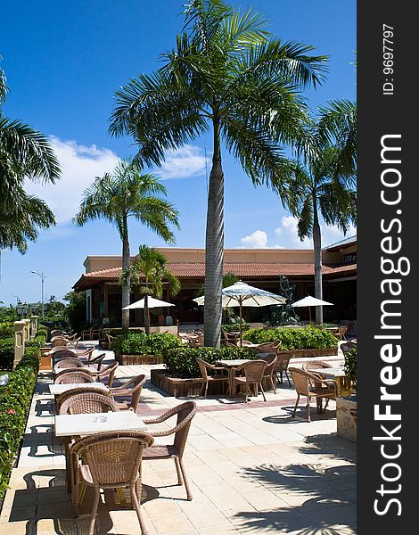 Tables and chairs on patio  in the hotel near bush grass palms blue sky. Tables and chairs on patio  in the hotel near bush grass palms blue sky