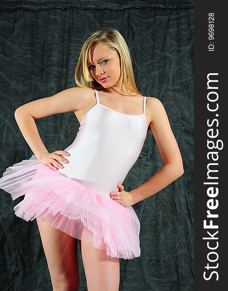 Young female dancer wearing a tutu standing against a black background.