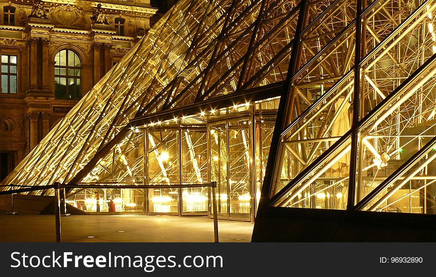 Metal Frame Glass Pyramid Outside A Museum With Yellow Lights During Nighttime