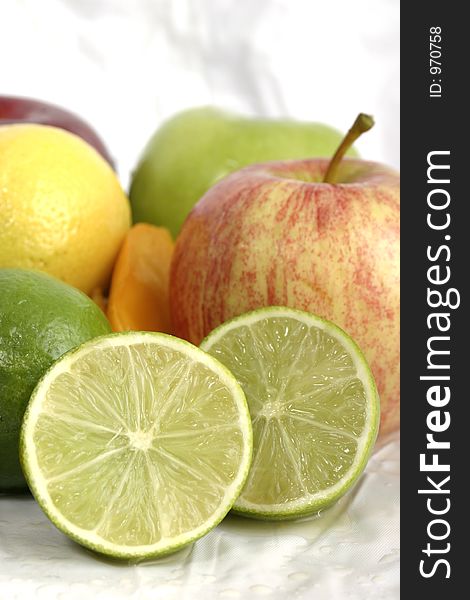 Close-up view of a sliced lime mixed in a group of other fruit on a white background. Close-up view of a sliced lime mixed in a group of other fruit on a white background.