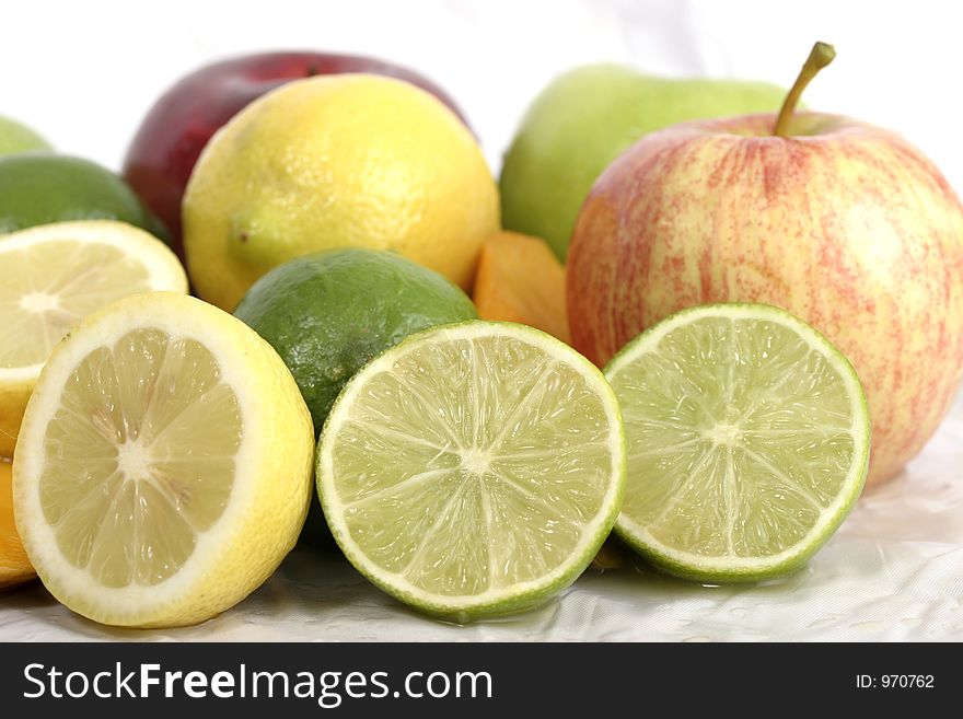 Close-up view of a sliced limes and lemons mixed in a group of other fruit on a white background. Close-up view of a sliced limes and lemons mixed in a group of other fruit on a white background.