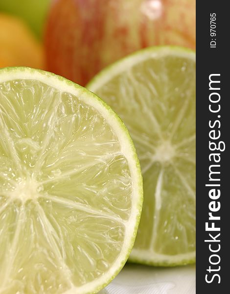 Extreme close-up view of two slices of lime and an apple and other fruit in the background. Extreme close-up view of two slices of lime and an apple and other fruit in the background.