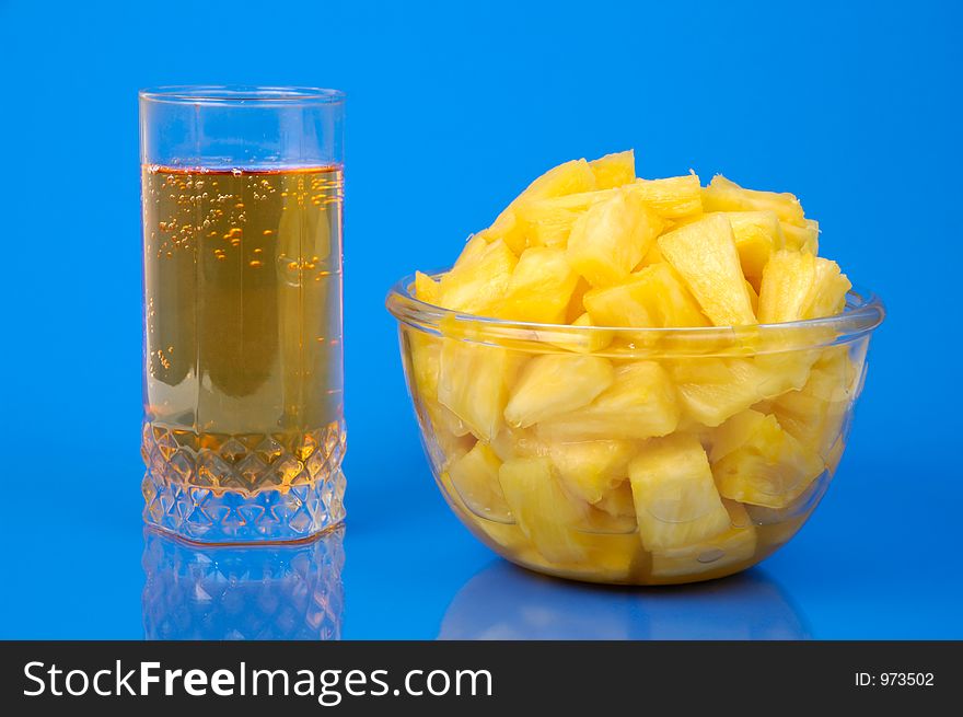 Pineapple pieces in bowl and glass of juice isolated on blue background. Pineapple pieces in bowl and glass of juice isolated on blue background