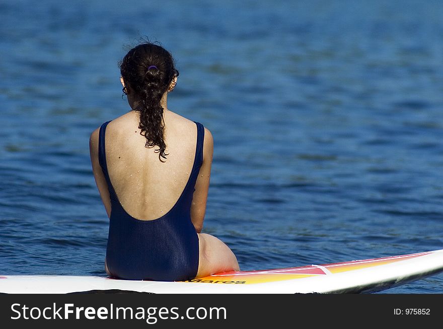 A teenager girl in a swimsuit sits floating on a surfboard looking out over the water. A teenager girl in a swimsuit sits floating on a surfboard looking out over the water.