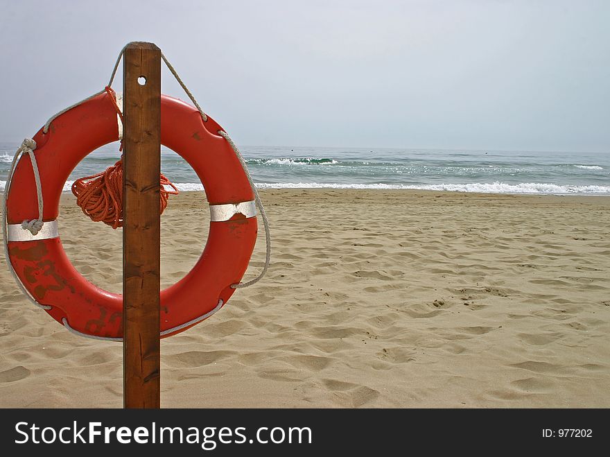 Orange life buoy hanging on a post on a sandy beach