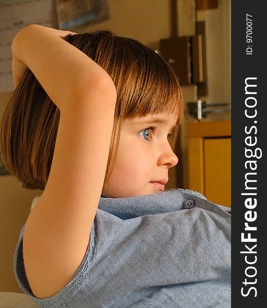 A young girl looks to the right, with her left arm behind her head.  Interior home, vertical portrait. A young girl looks to the right, with her left arm behind her head.  Interior home, vertical portrait.