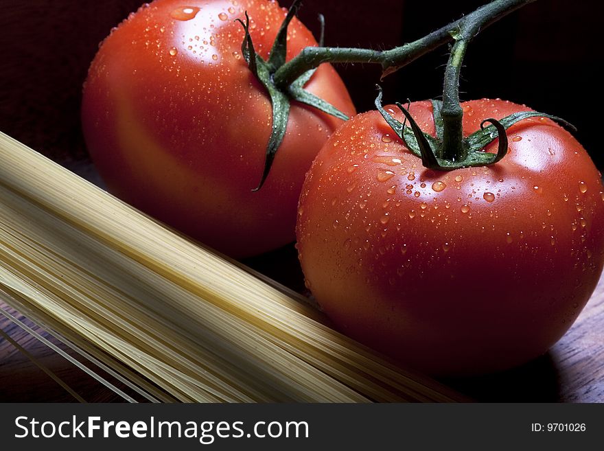 Red tomatos on a vine and pasta on dark background. Red tomatos on a vine and pasta on dark background