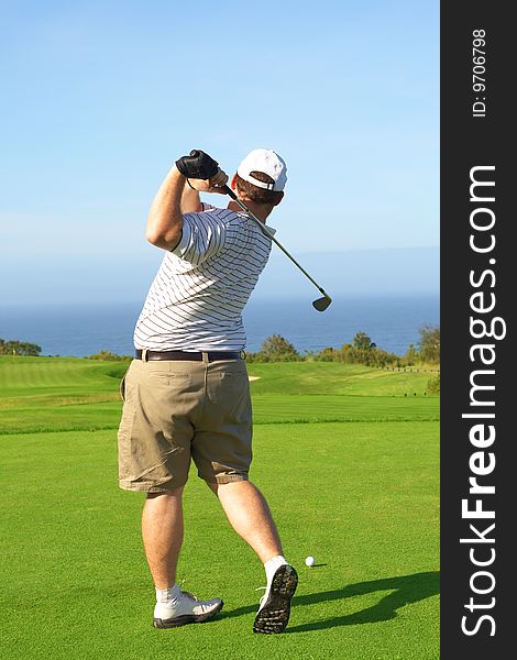 Young male golfer hitting the ball from the tee box next to the ocean on a beautiful summer day. Young male golfer hitting the ball from the tee box next to the ocean on a beautiful summer day