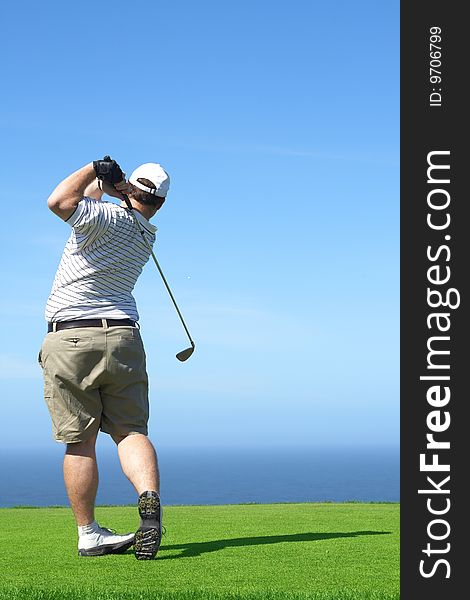 Young male golfer hitting the ball from the tee box next to the ocean on a beautiful summer day. Young male golfer hitting the ball from the tee box next to the ocean on a beautiful summer day