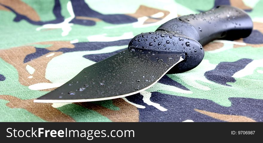 Black survivor knife with water drops on camouflage