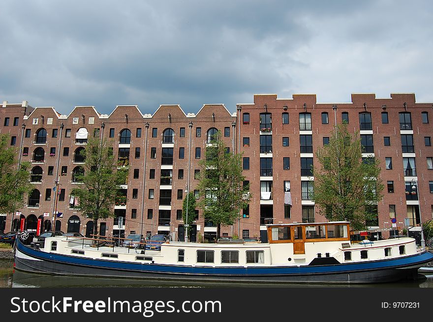 A living boat in front of some modern Canal Houses in Amsterdam with a grey sky background. A living boat in front of some modern Canal Houses in Amsterdam with a grey sky background...