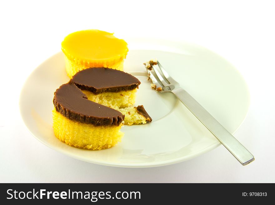 Two delicious looking cup cakes resting on a white plate with a fork on a plain background. Two delicious looking cup cakes resting on a white plate with a fork on a plain background