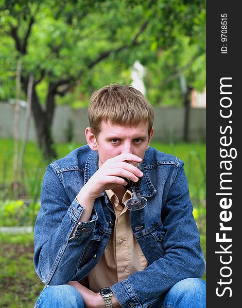 Young men in jeans jacket with glass of red wine in the garden. Young men in jeans jacket with glass of red wine in the garden