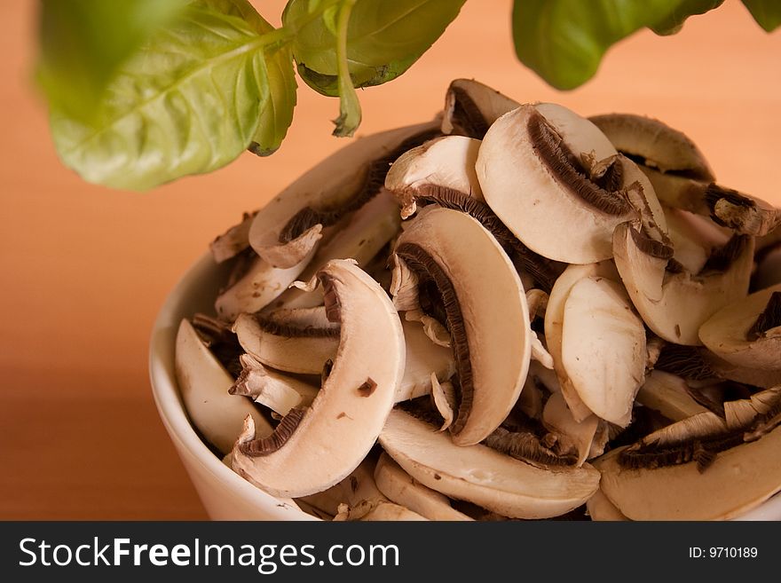 Freshly cut Champignons in white bowl under fresh Basilikum