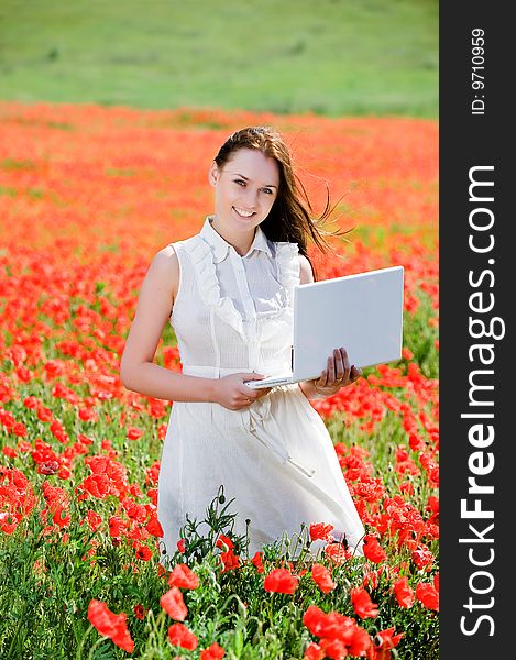 Attractive smiling girl with laptop in the poppy field