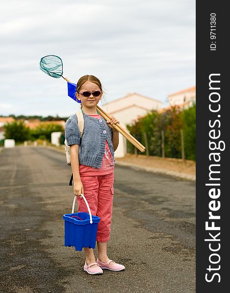 A girl pauses as she walks to the beach with a bucket, shovel, and net. A girl pauses as she walks to the beach with a bucket, shovel, and net.