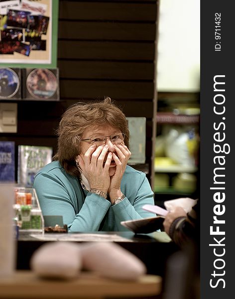 Older woman behind book sales counter looking perplexed with both hands up to face. Older woman behind book sales counter looking perplexed with both hands up to face.