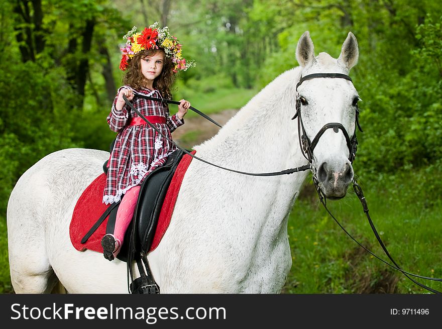 Little girl in floral wreath riding horse in the forest