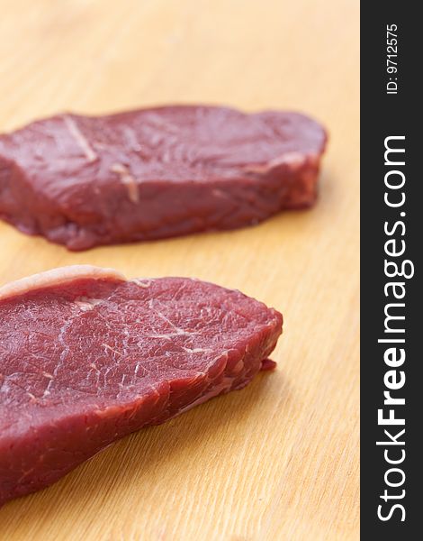 Uncooked steaks on wooden cutting board.