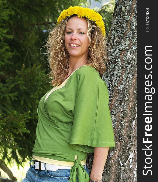 Curly girl with dandelion chain on head standing by birch tree