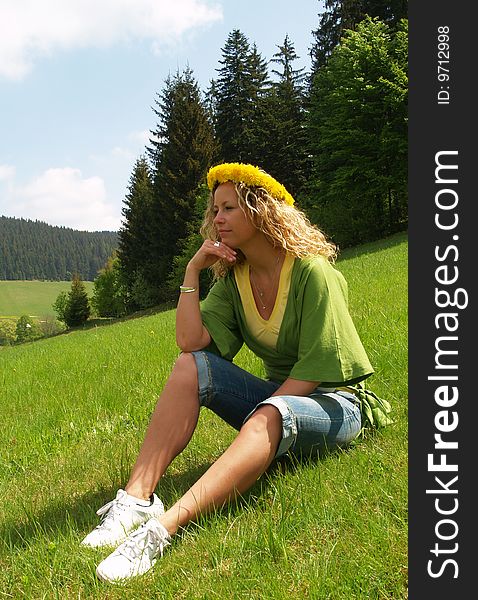 Curly girl with dandelion chain on head sitting on meadow