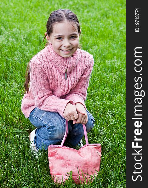 Girl in a pink sweater sits on a green grass