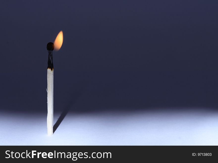 A lone burning match standing on gradient background. Horizontal image