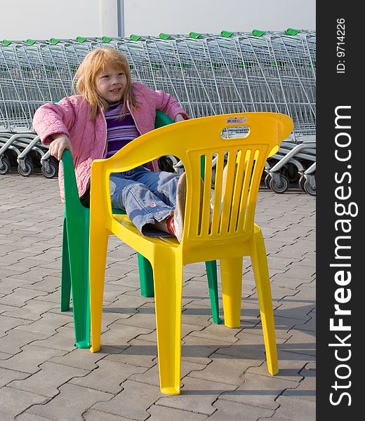 The red girl on a plastic chair on a background of a supermarket and store carriages