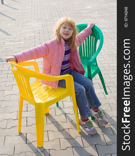 The girl and two plastic chairs on sidewalk from a concrete tile