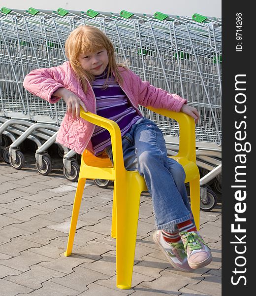 The red girl on a plastic chair on a background of a supermarket and store carriages