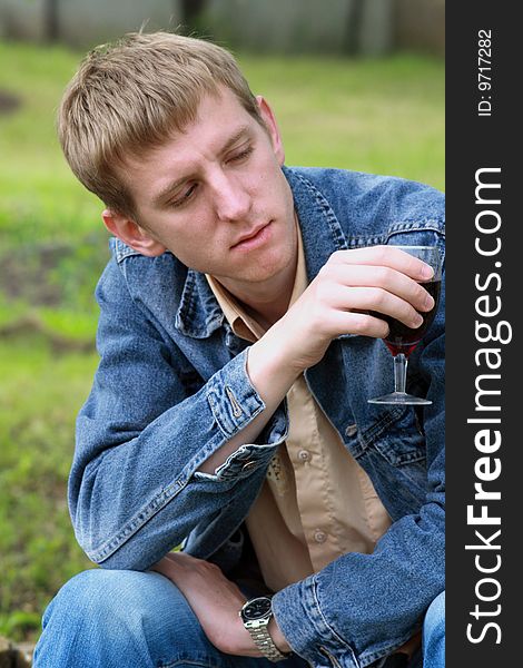 Young men in jeans jacket with glass of red wine in the garden. Young men in jeans jacket with glass of red wine in the garden