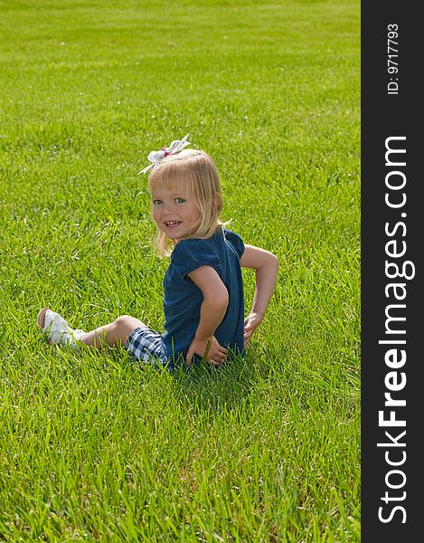 Little blond girl sitting in grass turning to smile at camera. Little blond girl sitting in grass turning to smile at camera