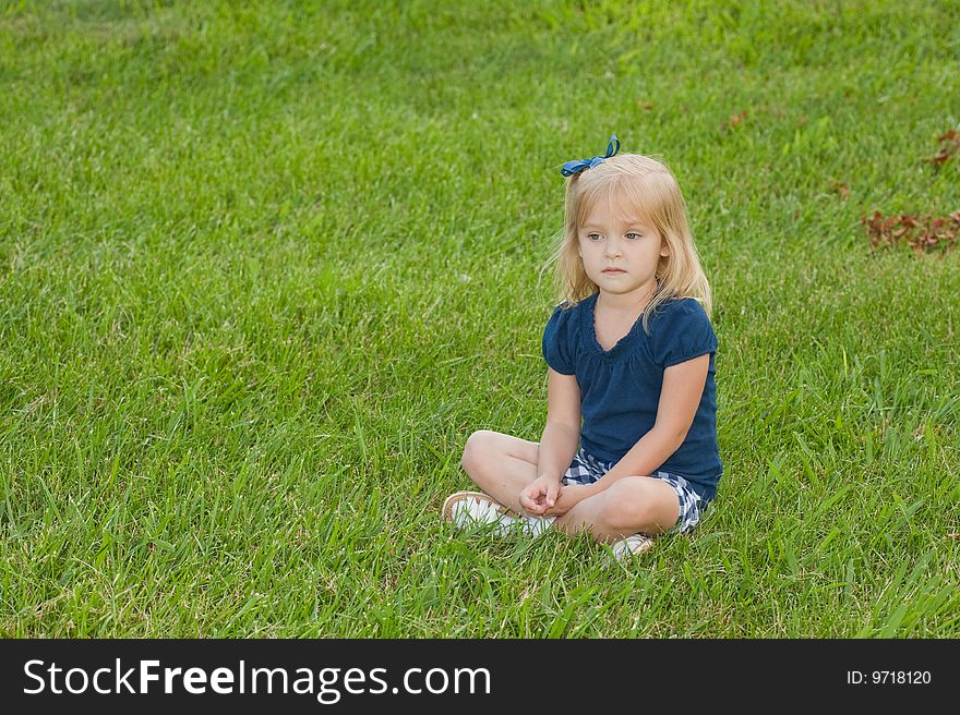 One blond girl sitting in grass with a contemplative look on her face. One blond girl sitting in grass with a contemplative look on her face