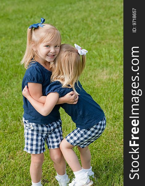 Two little blond girls in grass hugging each other. Two little blond girls in grass hugging each other