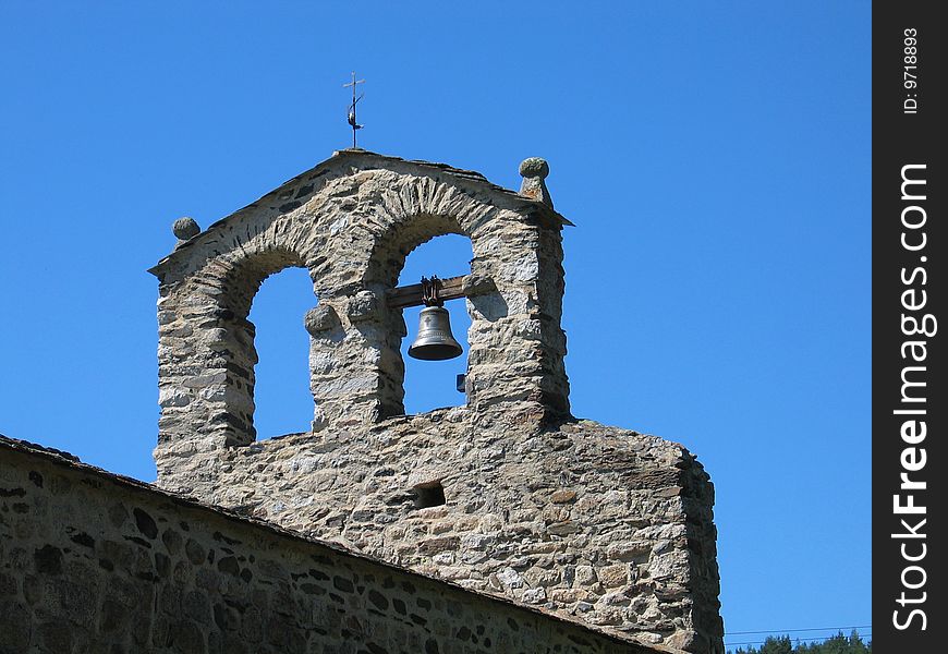 Stone belltower with single bell against clear blue sky