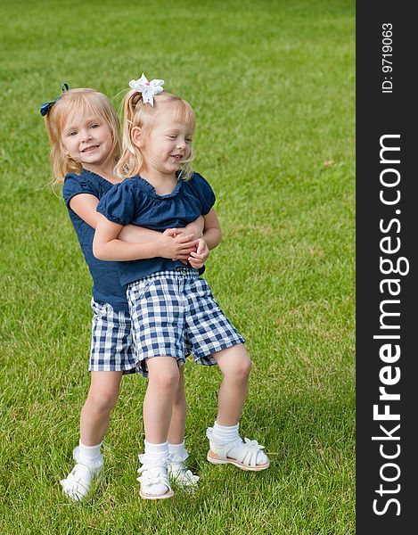 Two little blond girls in grass hugging each other. Two little blond girls in grass hugging each other