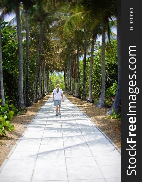 A woman enjoys a walk through a beautiful palm tree-lined path at a beautiful tropical resort. (Selective focus on the woman). A woman enjoys a walk through a beautiful palm tree-lined path at a beautiful tropical resort. (Selective focus on the woman)