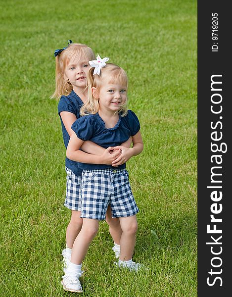 Two little blond girls in grass hugging each other. Two little blond girls in grass hugging each other