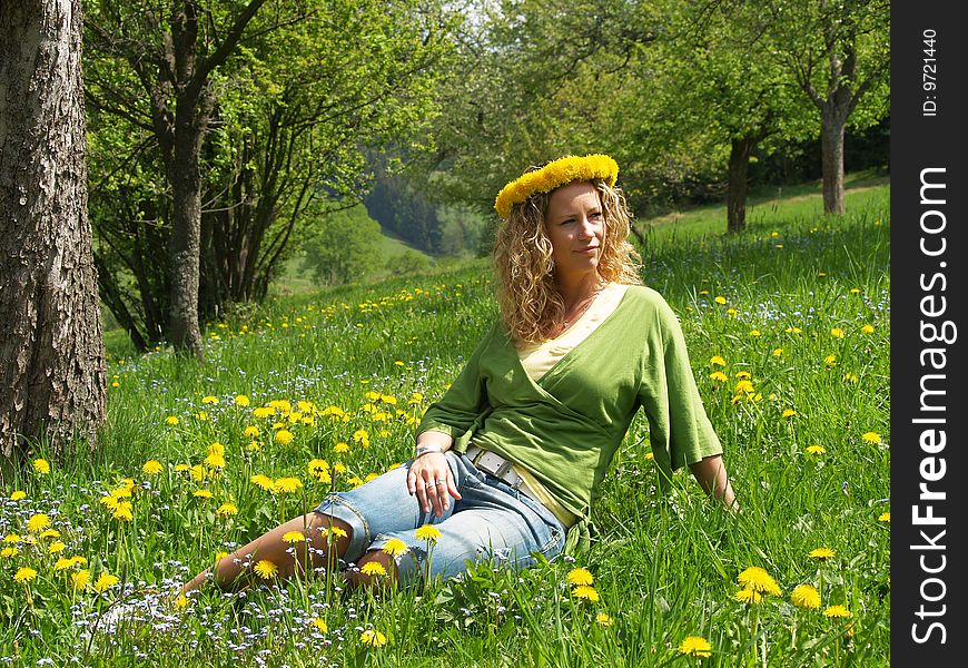 Curly girl with dandelion chain on head sitting in orchard