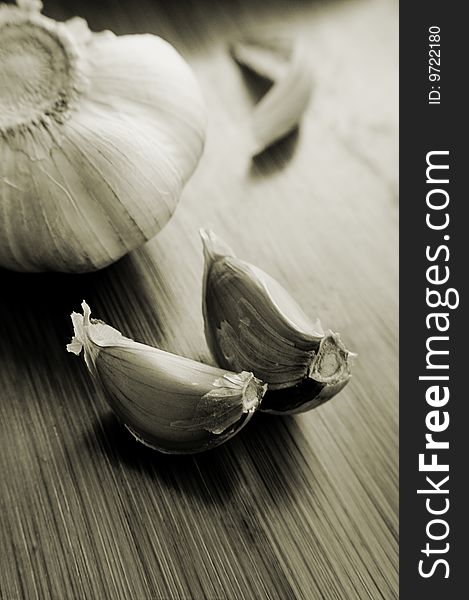 Garlic bulb and its slices on wooden texture, sepia